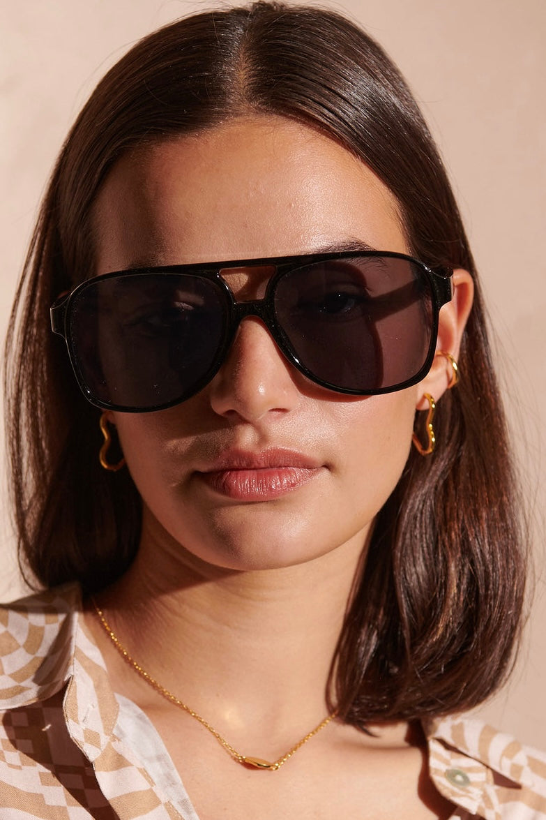  Woman in oversized black sunglasses with gold hoop earrings and patterned blouse - modern boho street style Australia.