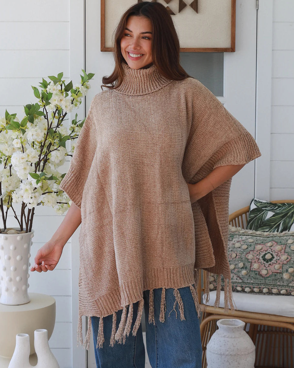 Warm oat roll neck knit poncho with fringe hem draped winter layering piece styled over fitted long sleeve neutral outfit Australia