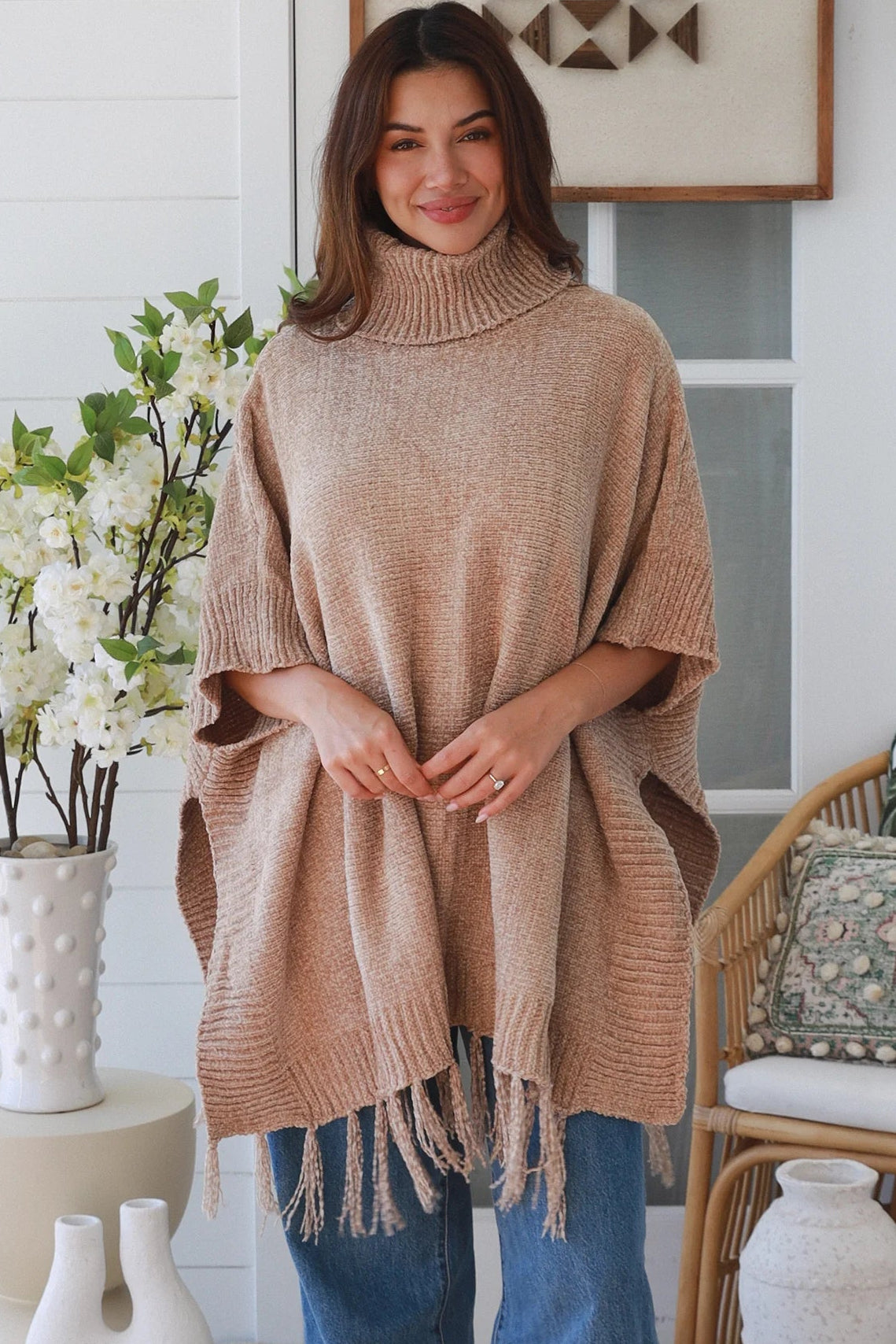 Warm oat roll neck knit poncho with fringe hem draped winter layering piece styled over fitted long sleeve neutral outfit Australia