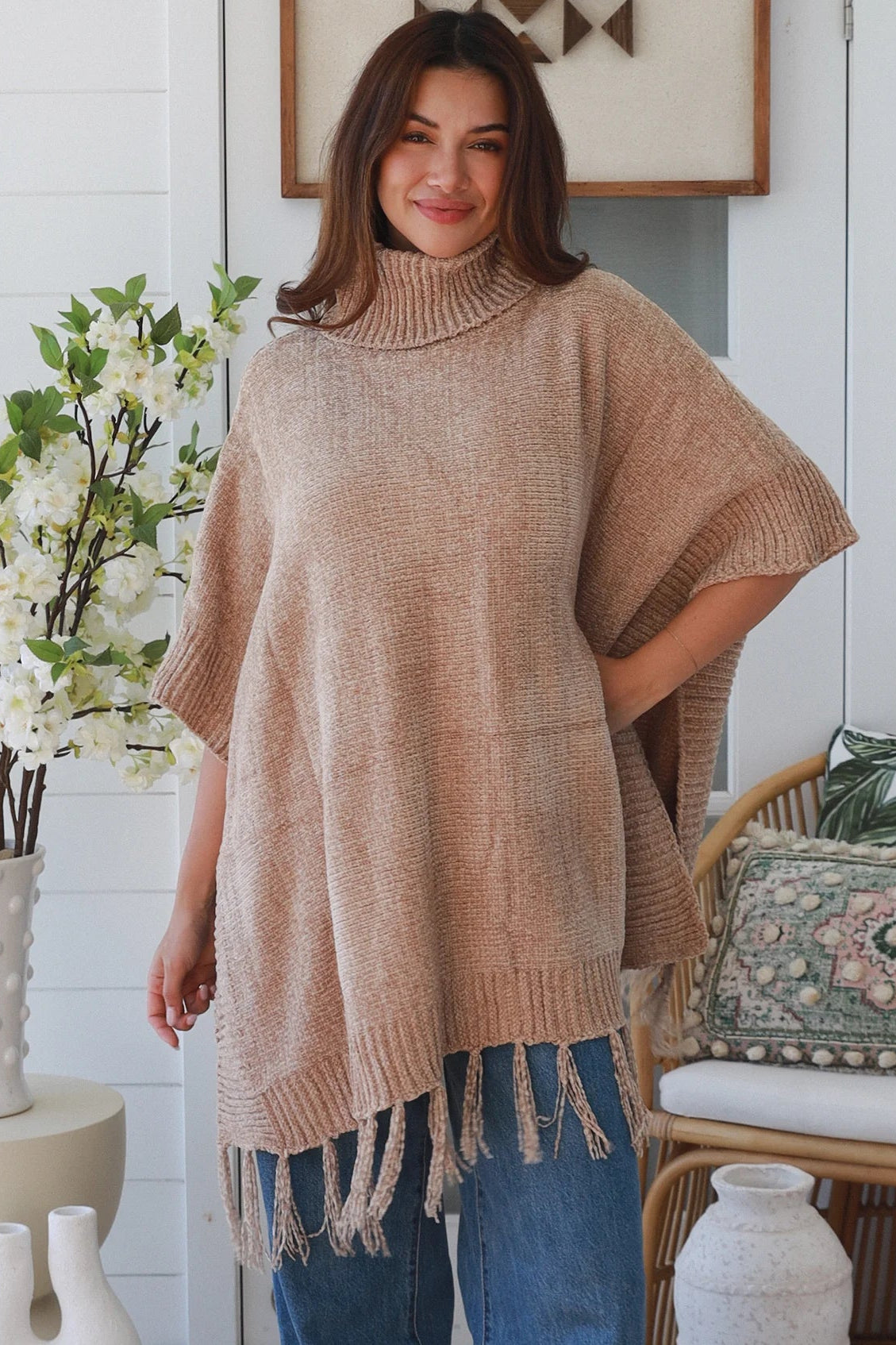 Warm oat roll neck knit poncho with fringe hem draped winter layering piece styled over fitted long sleeve neutral outfit Australia
