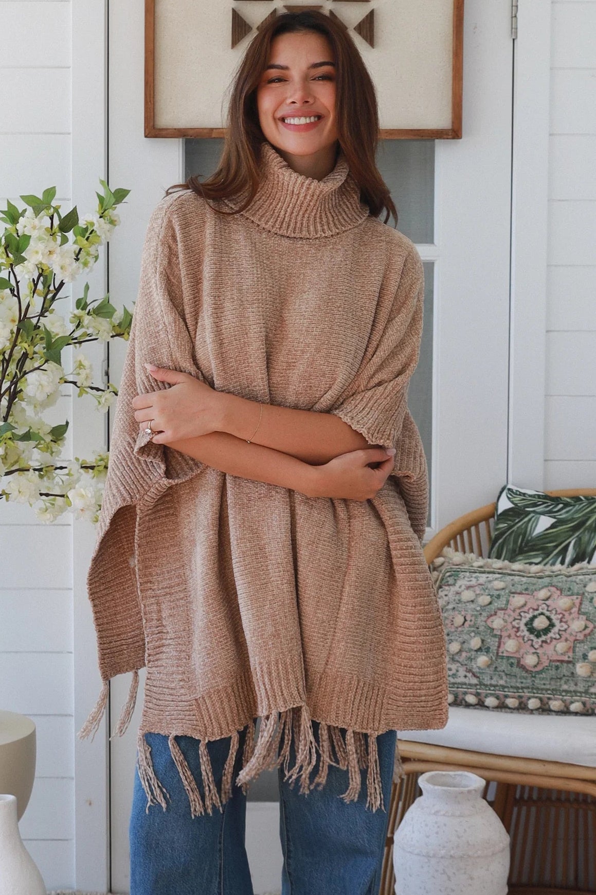 Warm oat roll neck knit poncho with fringe hem draped winter layering piece styled over fitted long sleeve neutral outfit Australia