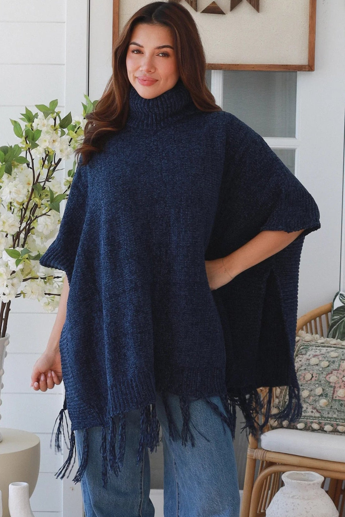 Woman wearing navy roll neck knit poncho with fringe hem and relaxed winter boho styling