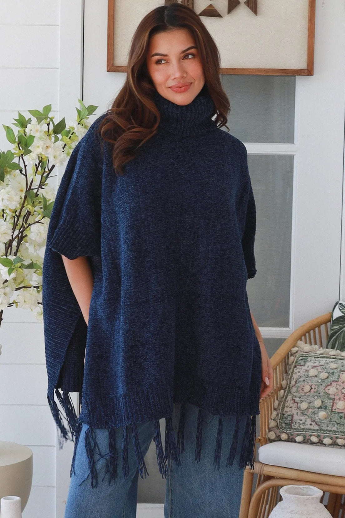 Woman wearing navy roll neck knit poncho with fringe hem and relaxed winter boho styling