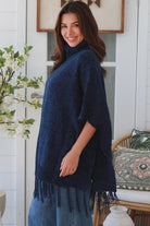 Woman wearing navy roll neck knit poncho with fringe hem and relaxed winter boho styling