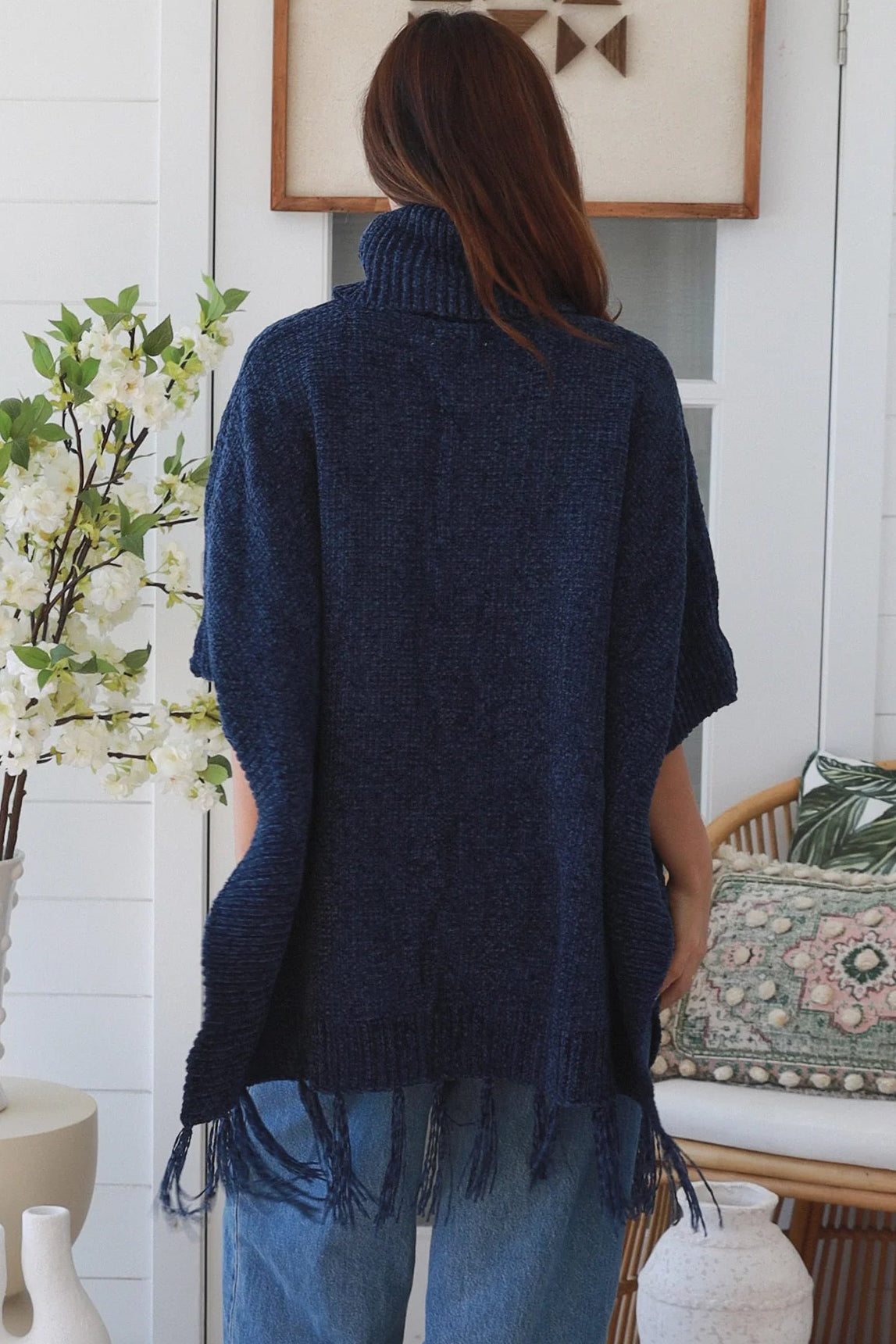 Woman wearing navy roll neck knit poncho with fringe hem and relaxed winter boho styling