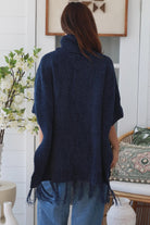 Woman wearing navy roll neck knit poncho with fringe hem and relaxed winter boho styling