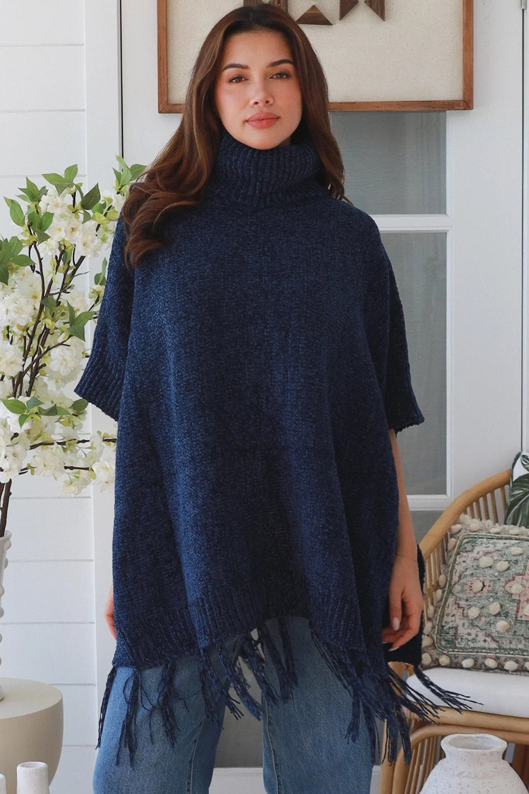Woman wearing navy roll neck knit poncho with fringe hem and relaxed winter boho styling