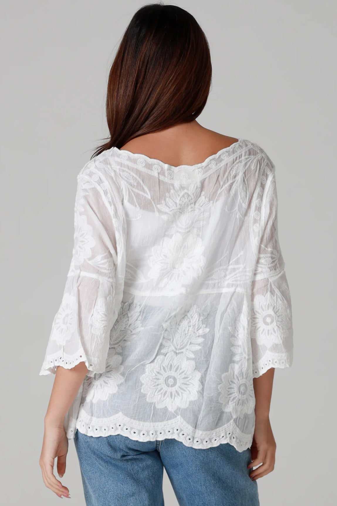 Woman wearing a white cotton embroidered boho blouse with scalloped neckline and flared sleeves styled with denim jeans - Fleur Belle Blouse Australia.