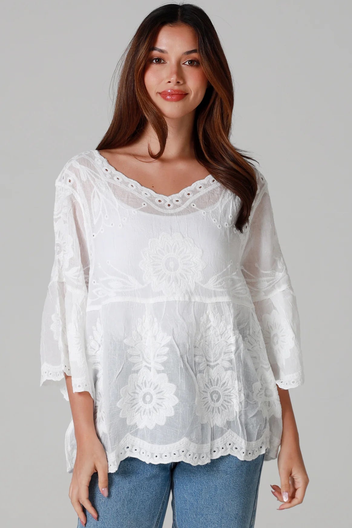 Woman wearing a white cotton embroidered boho blouse with scalloped neckline and flared sleeves styled with denim jeans - Fleur Belle Blouse Australia.