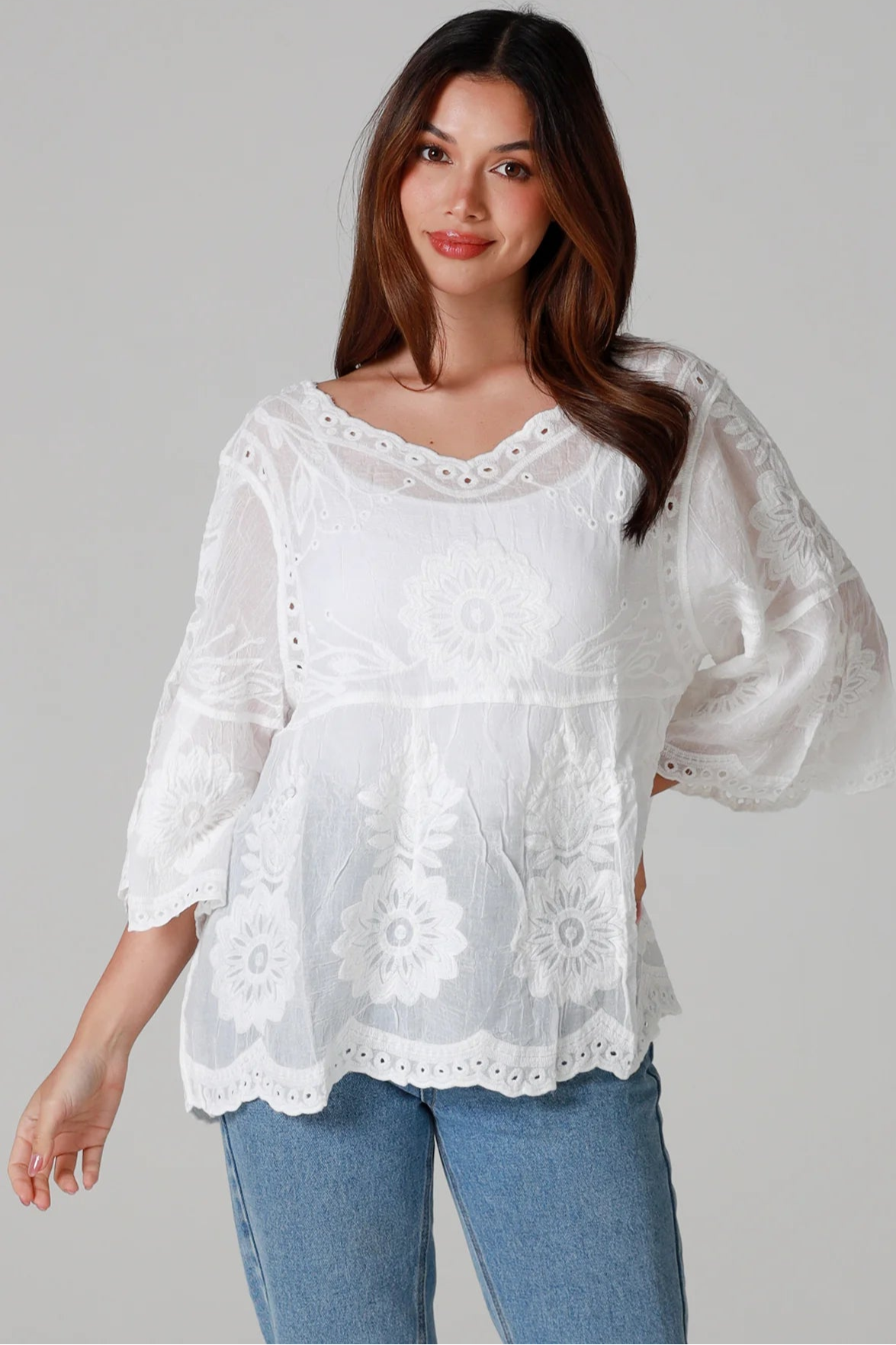 Woman wearing a white cotton embroidered boho blouse with scalloped neckline and flared sleeves styled with denim jeans - Fleur Belle Blouse Australia.