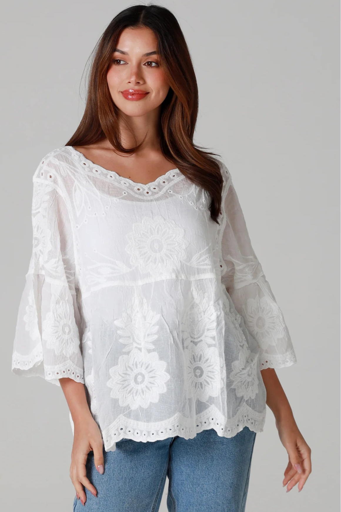 Woman wearing a white cotton embroidered boho blouse with scalloped neckline and flared sleeves styled with denim jeans - Fleur Belle Blouse Australia.