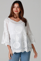 Woman wearing a white cotton embroidered boho blouse with scalloped neckline and flared sleeves styled with denim jeans - Fleur Belle Blouse Australia.