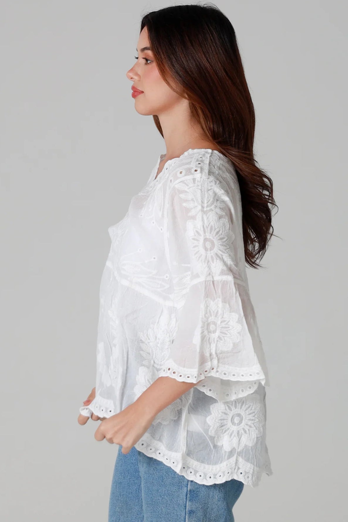 Woman wearing a white cotton embroidered boho blouse with scalloped neckline and flared sleeves styled with denim jeans - Fleur Belle Blouse Australia.