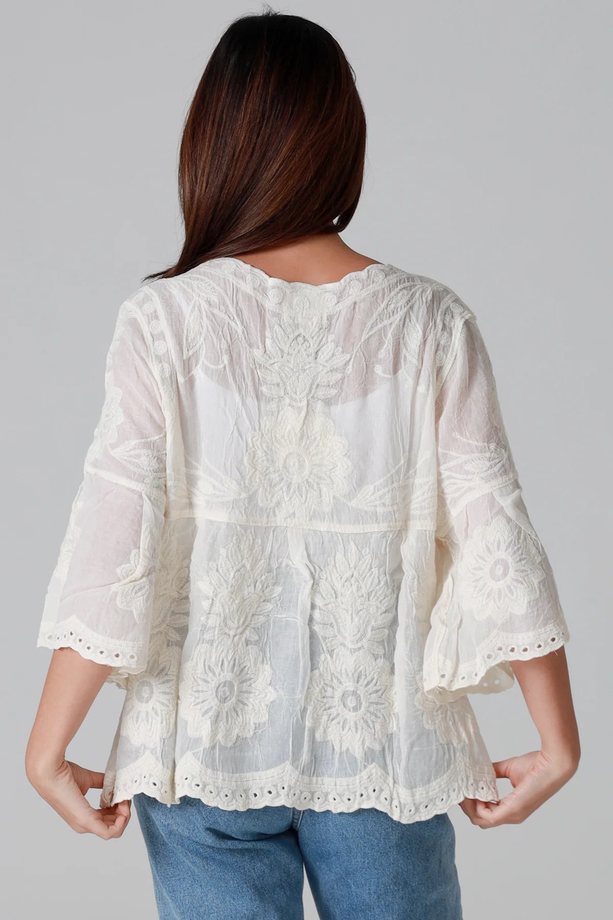 Woman wearing a cream embroidered cotton blouse with flared sleeves and scalloped neckline styled with jeans - Fleur Belle Blouse Australia.