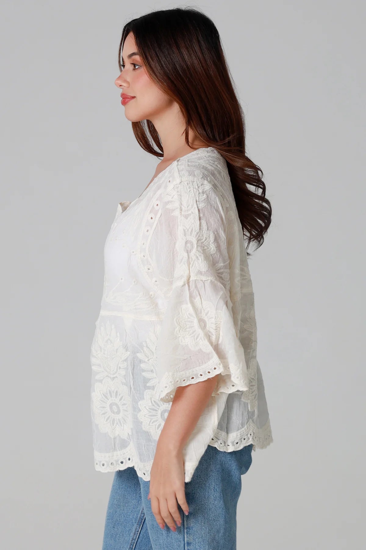 Woman wearing a cream embroidered cotton blouse with flared sleeves and scalloped neckline styled with jeans - Fleur Belle Blouse Australia.