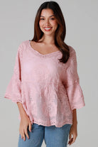 Woman wearing a blush pink embroidered cotton blouse with scalloped neckline and flared sleeves, styled with denim jeans - romantic boho top Australia.