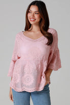 Woman wearing a blush pink embroidered cotton blouse with scalloped neckline and flared sleeves, styled with denim jeans - romantic boho top Australia.