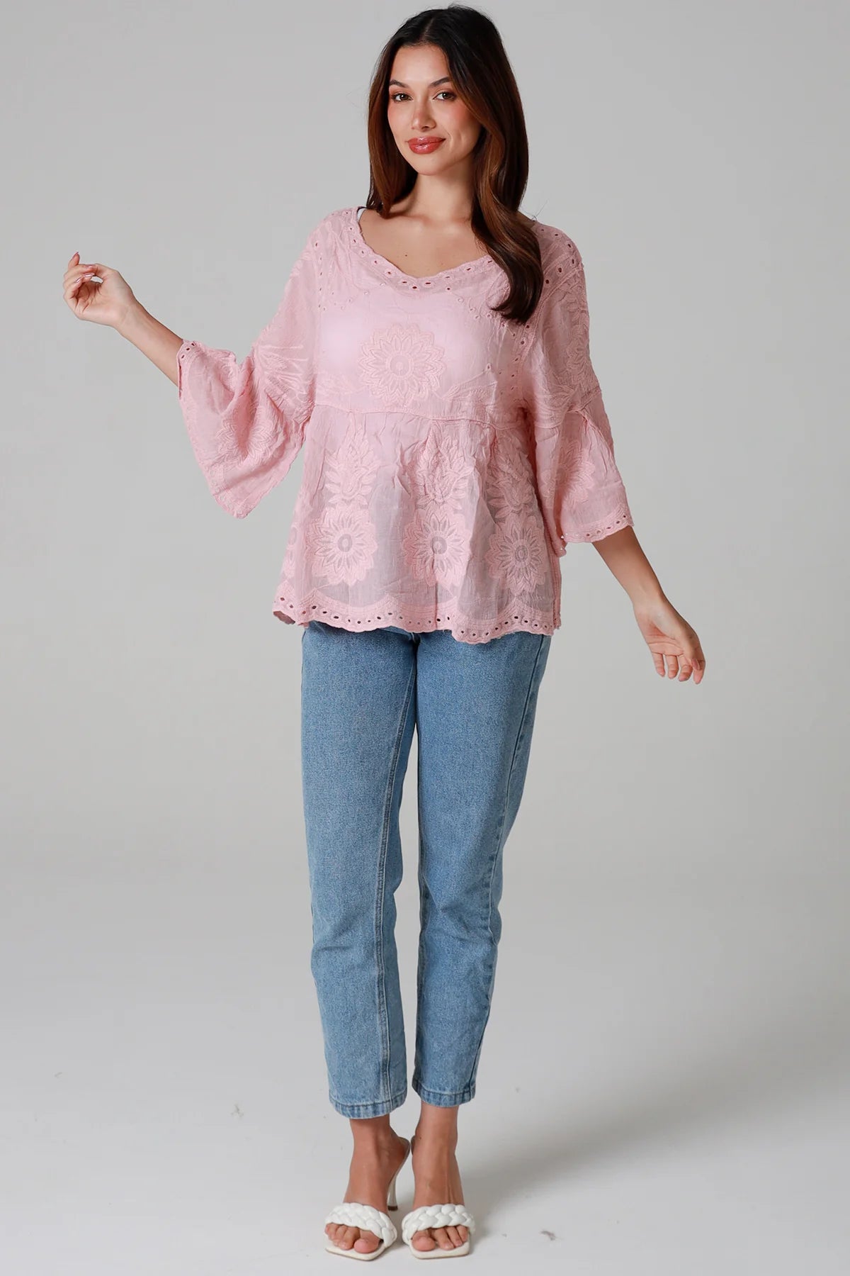 Woman wearing a blush pink embroidered cotton blouse with scalloped neckline and flared sleeves, styled with denim jeans - romantic boho top Australia.