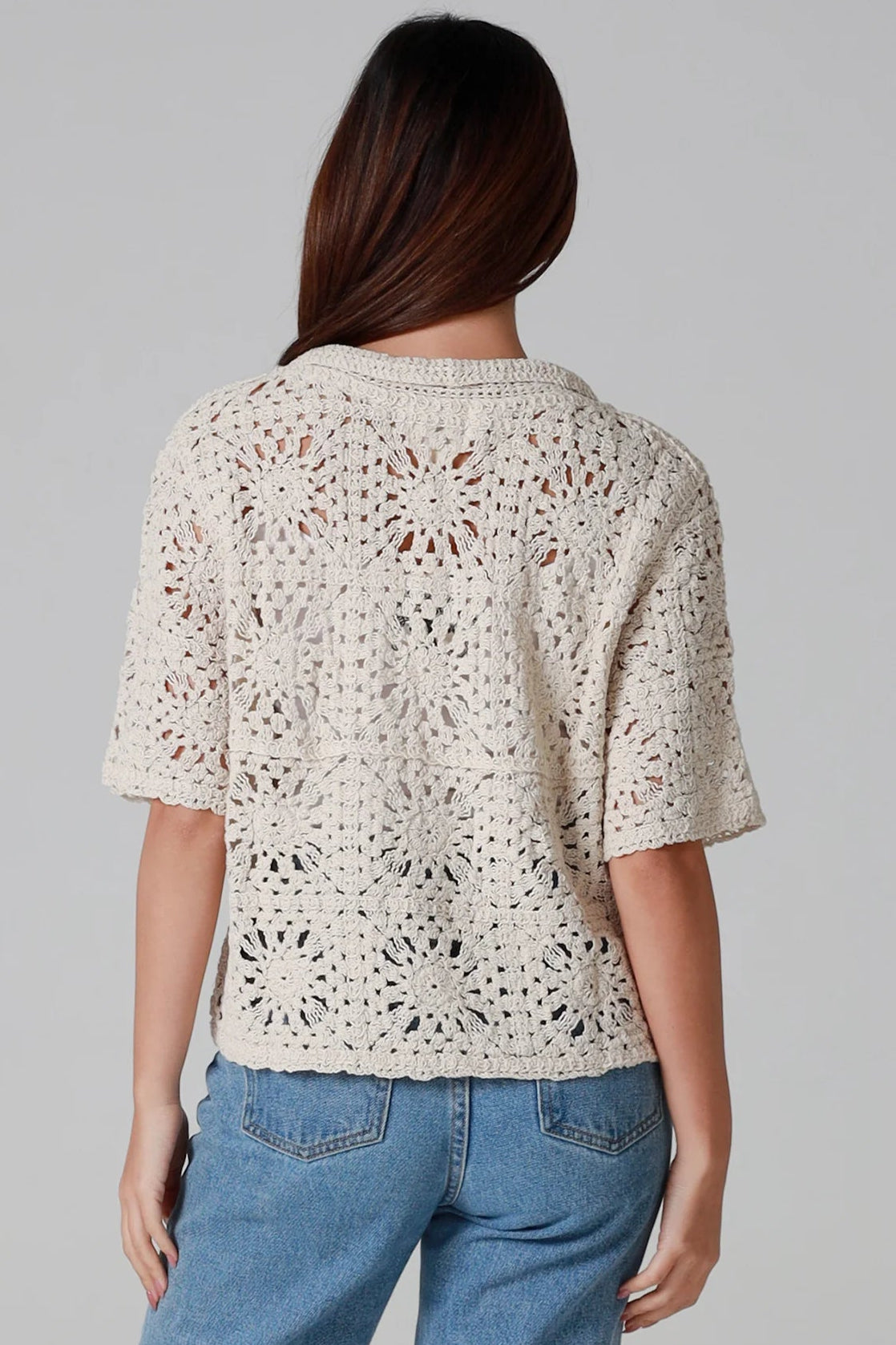 Woman wearing a beige short-sleeve crochet blouse with scalloped collar and buttons, styled open over jeans - boho cardigan top Australia.
