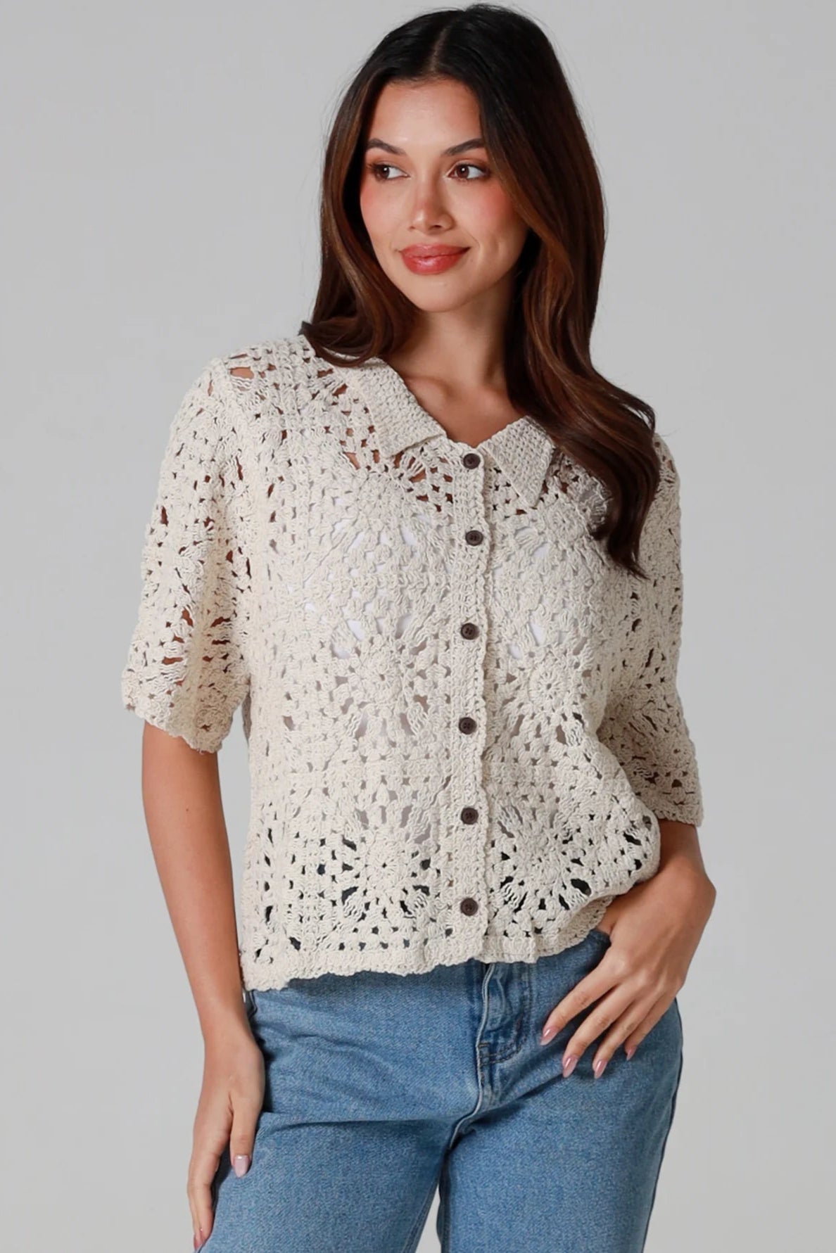 Woman wearing a beige short-sleeve crochet blouse with scalloped collar and buttons, styled open over jeans - boho cardigan top Australia.