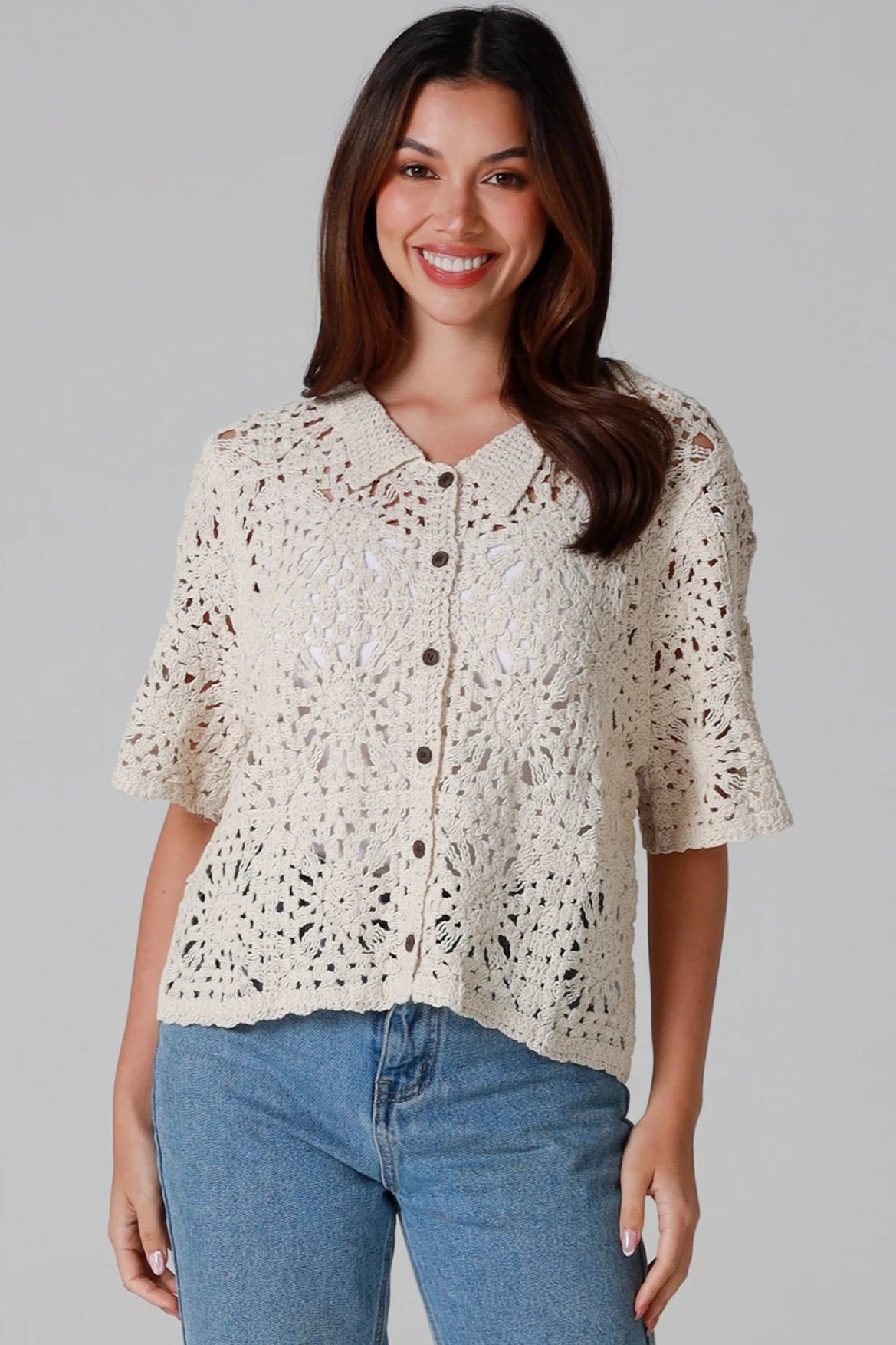 Woman wearing a beige short-sleeve crochet blouse with scalloped collar and buttons, styled open over jeans - boho cardigan top Australia.
