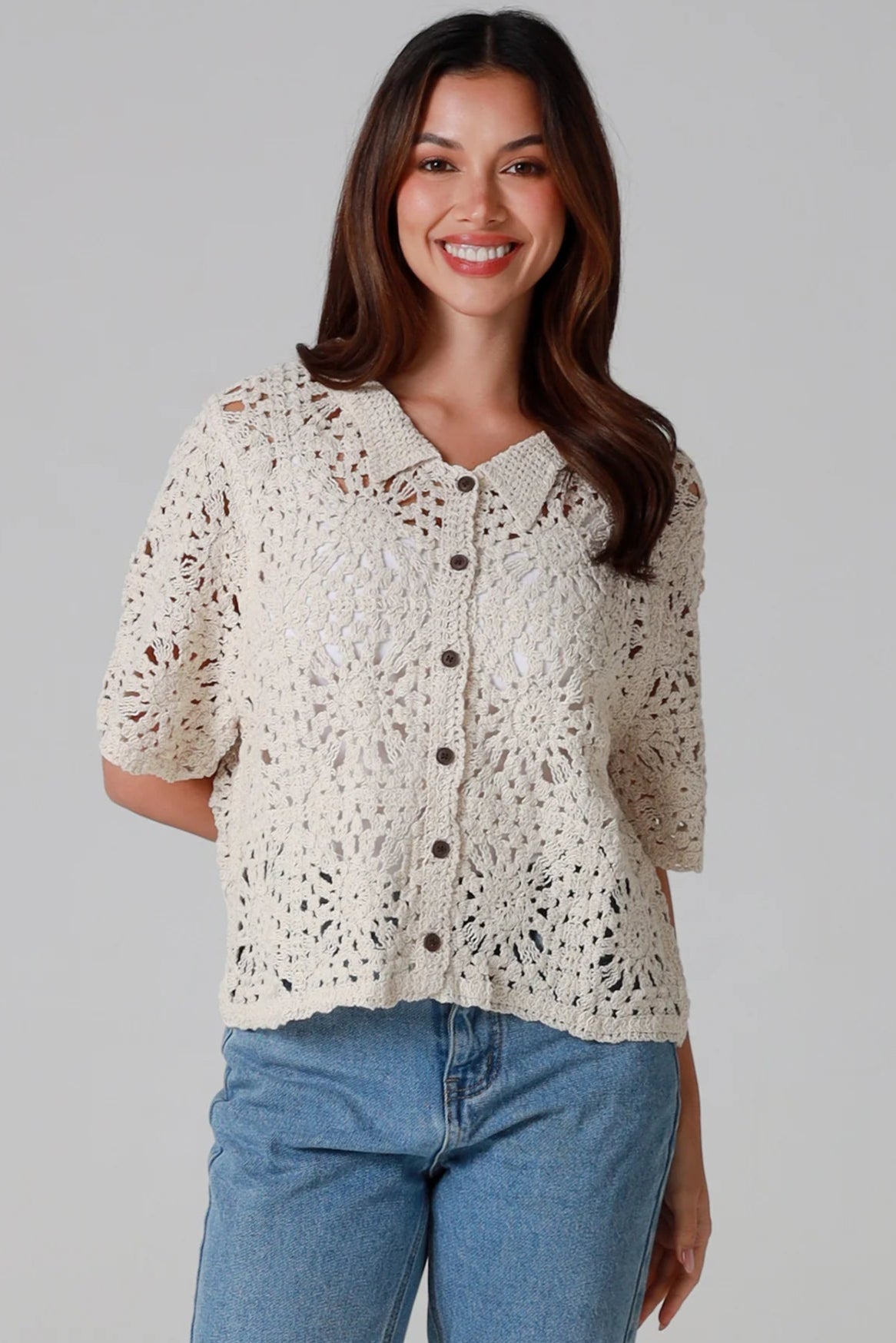 Woman wearing a beige short-sleeve crochet blouse with scalloped collar and buttons, styled open over jeans - boho cardigan top Australia.