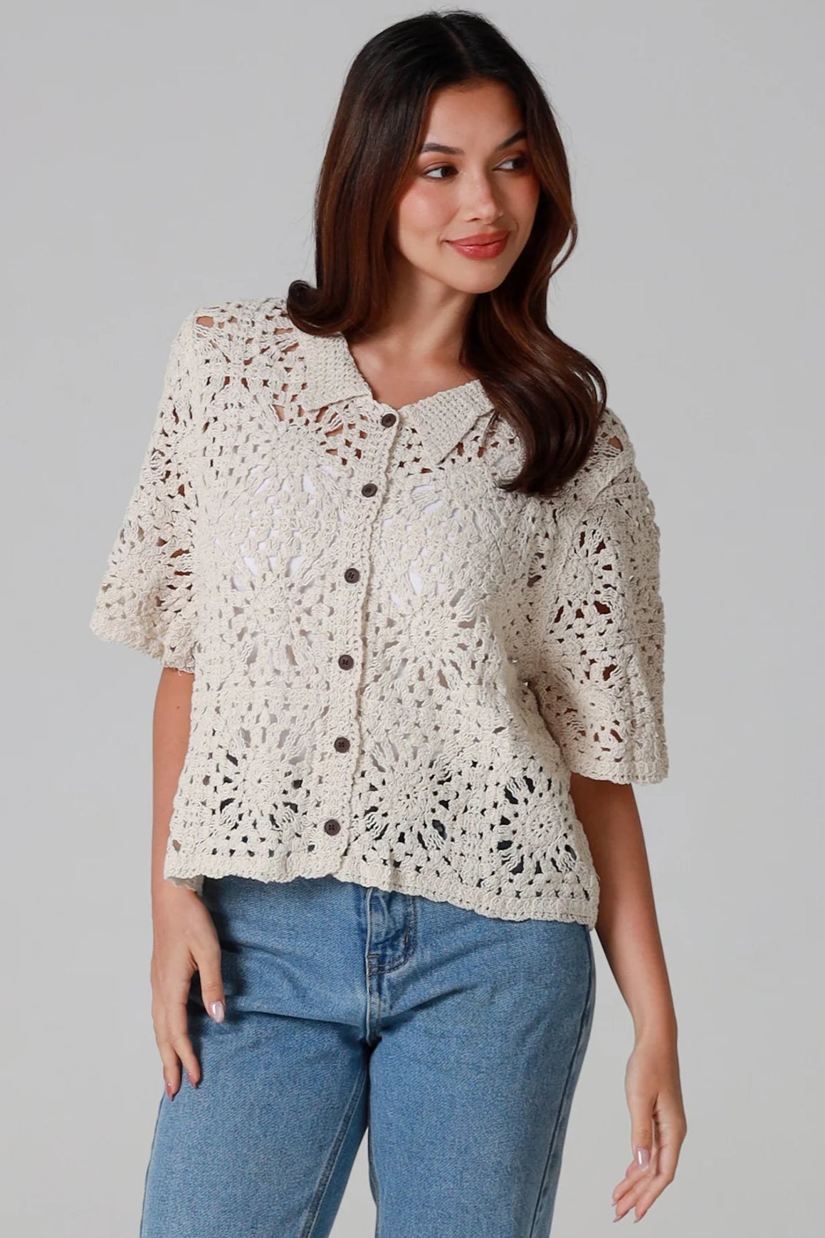 Woman wearing a beige short-sleeve crochet blouse with scalloped collar and buttons, styled open over jeans - boho cardigan top Australia.