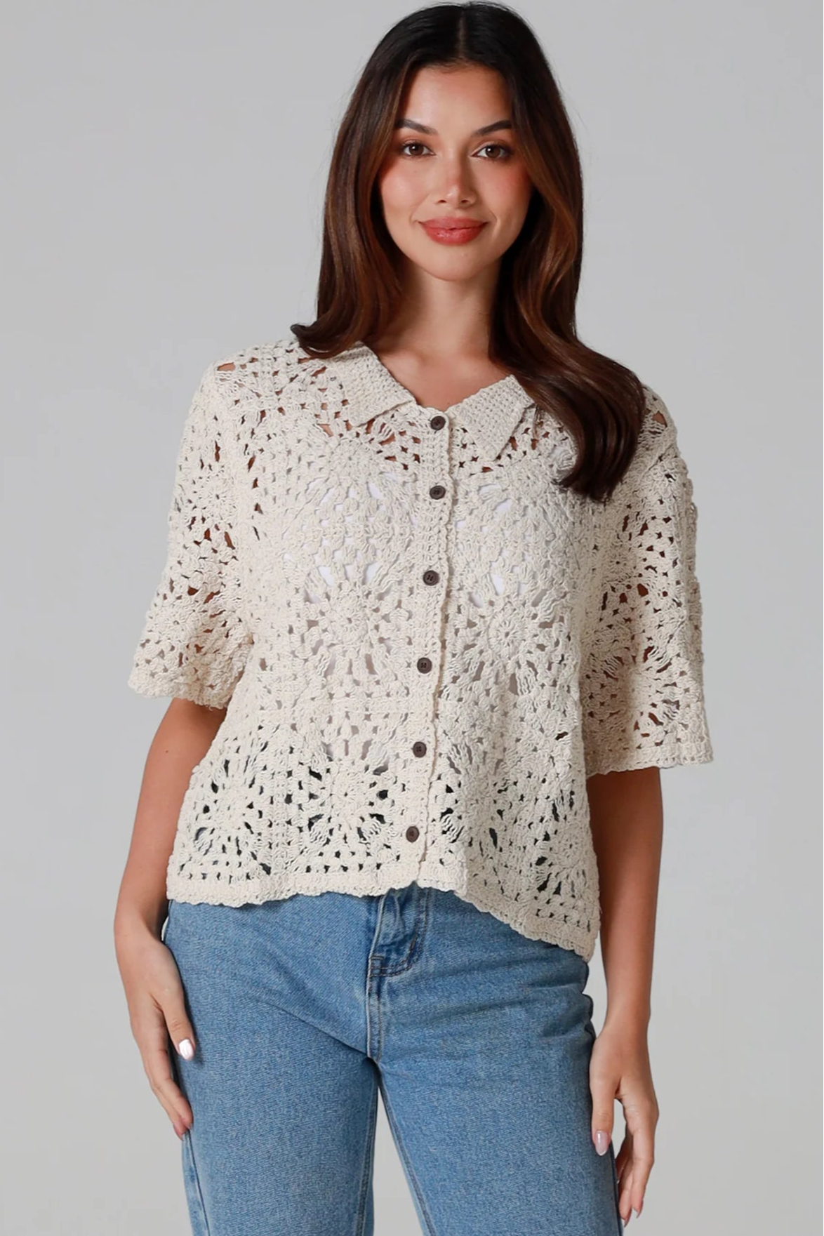 Woman wearing a beige short-sleeve crochet blouse with scalloped collar and buttons, styled open over jeans - boho cardigan top Australia.
