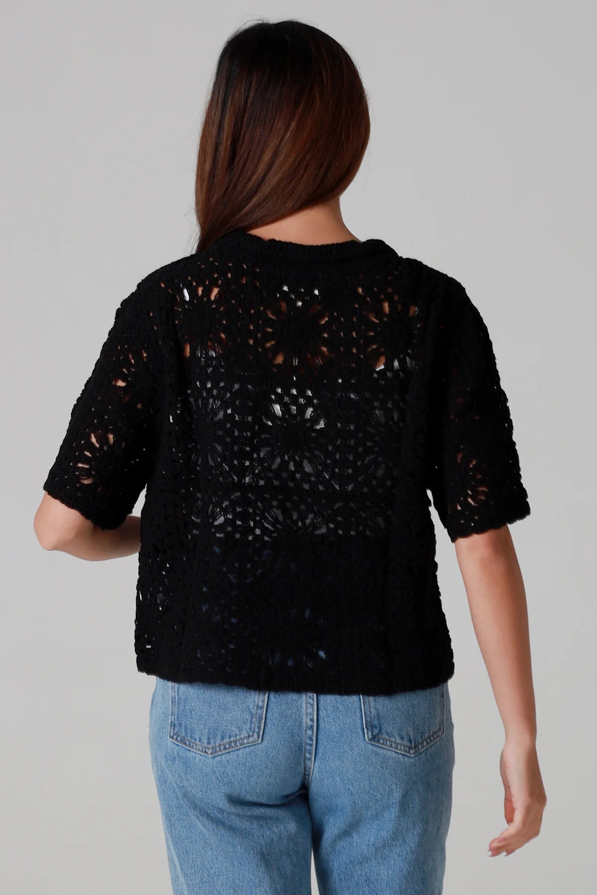 Woman wearing a black cotton crochet cardigan with collar and short sleeves styles with light blue jeans - boho crochet top Australia.