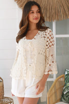 Woman wearing a cream crochet cotton cardigan with floral and diamond pattern and scalloped sleeves - boho fashion Australia