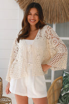 Woman wearing a cream crochet cotton jacket with bell sleeves and tie-front - boho layering piece Australia