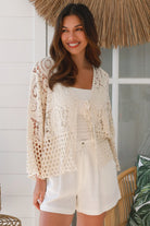 Woman wearing a cream crochet cotton jacket with bell sleeves and tie-front - boho layering piece Australia