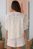Woman wearing a cream embroidered cotton blouse with artisan trim – Zoe Embroidered Cotton Top Cream.