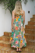 Woman in colourful ankle-sweeping island-print boho maxi dress with frill hemline and adjustable straps in bright summer.