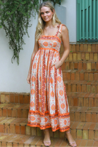 Woman wearing a sunset-coloured ankle-length maxi dress with shoulder ties and zigzag trim – Sundown Spice Maxi Dress.
