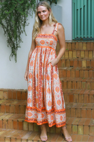 Woman wearing a sunset-coloured ankle-length maxi dress with shoulder ties and zigzag trim – Sundown Spice Maxi Dress.