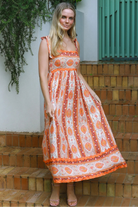 Woman wearing a sunset-coloured ankle-length maxi dress with shoulder ties and zigzag trim – Sundown Spice Maxi Dress.