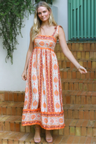 Woman wearing a sunset-coloured ankle-length maxi dress with shoulder ties and zigzag trim – Sundown Spice Maxi Dress.