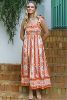 Woman wearing a sunset-coloured ankle-length maxi dress with shoulder ties and zigzag trim – Sundown Spice Maxi Dress.