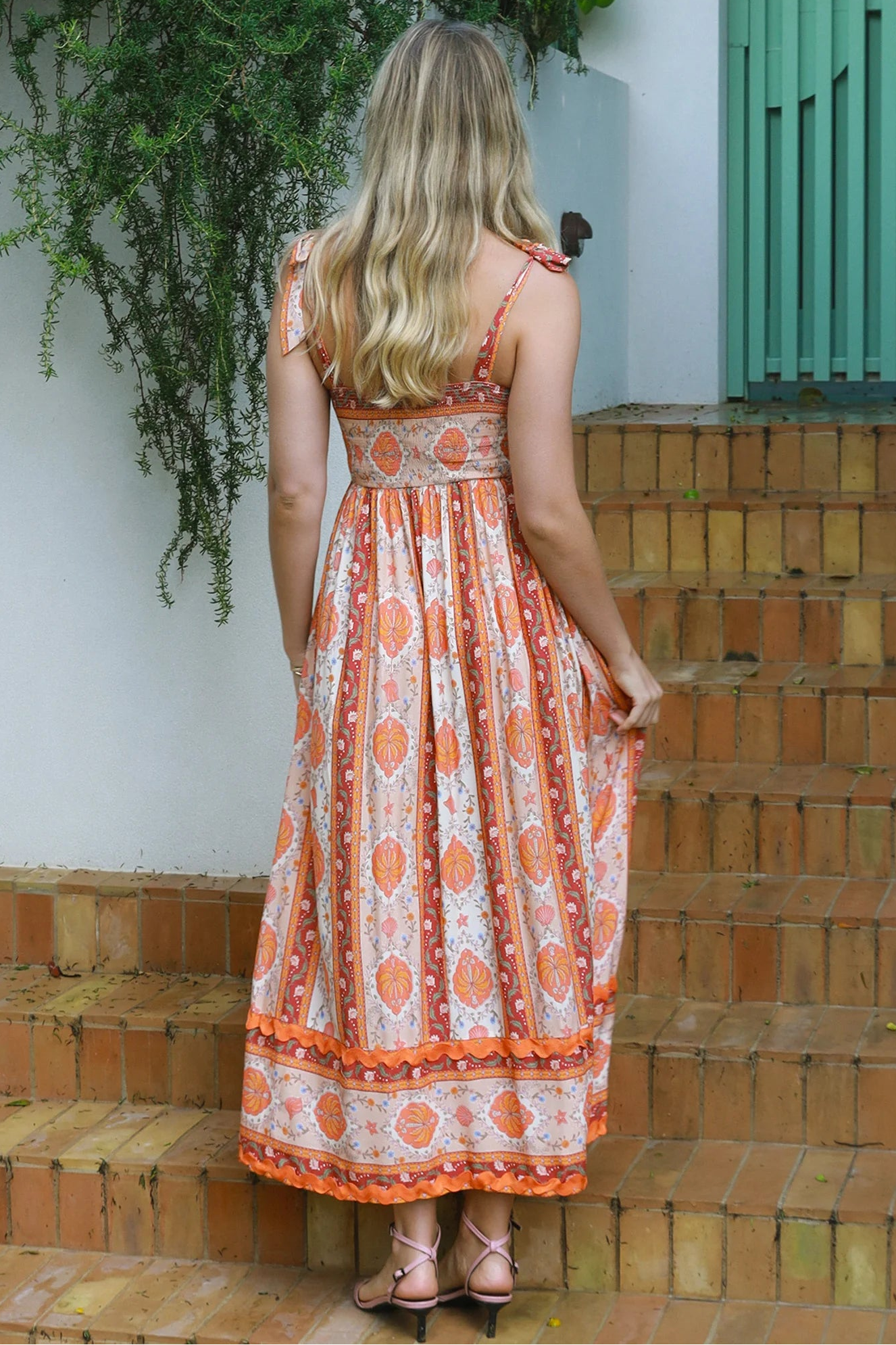 Woman wearing a sunset-coloured ankle-length maxi dress with shoulder ties and zigzag trim – Sundown Spice Maxi Dress.