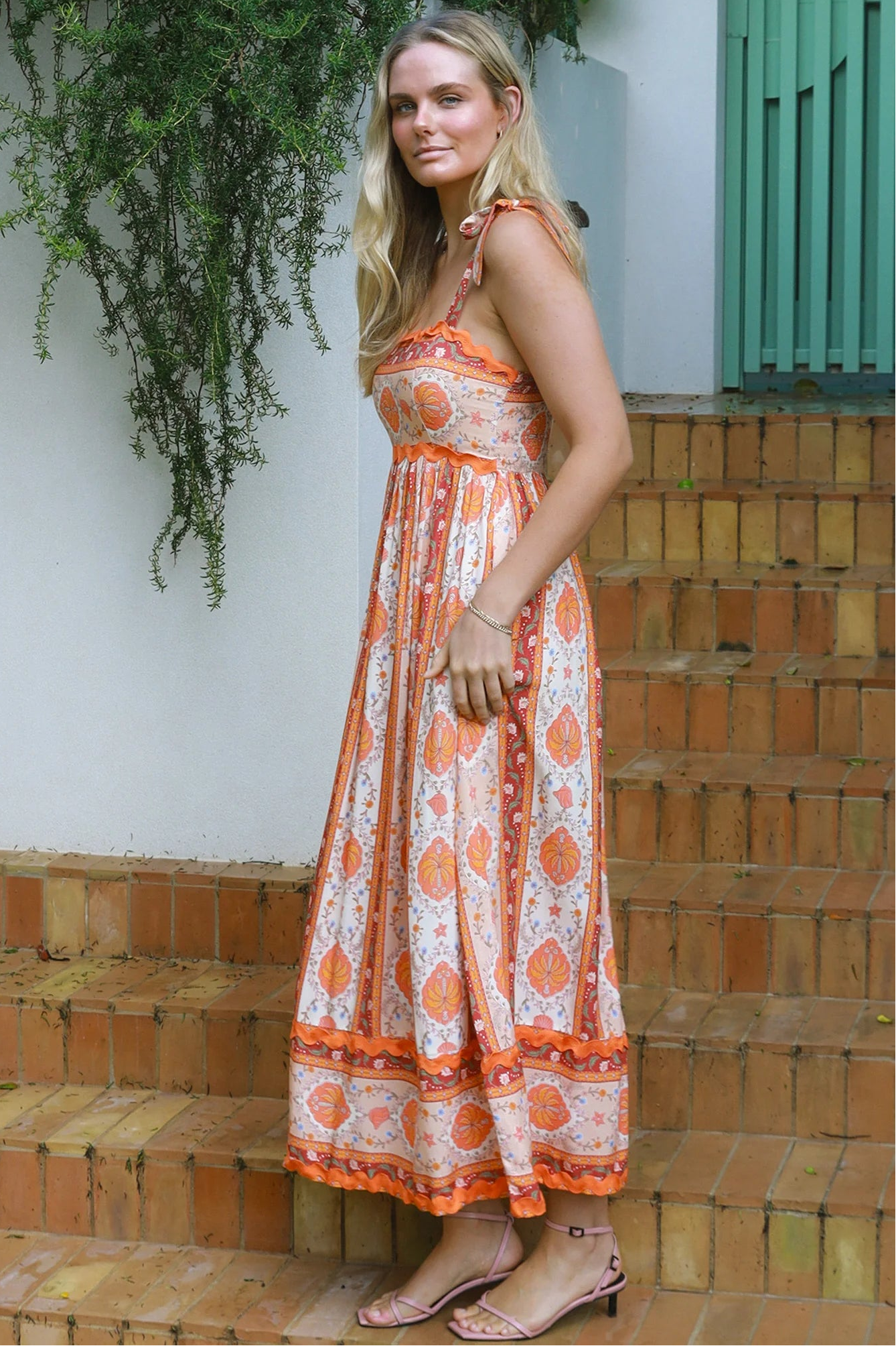 Woman wearing a sunset-coloured ankle-length maxi dress with shoulder ties and zigzag trim – Sundown Spice Maxi Dress.