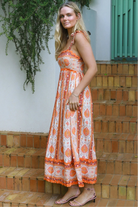 Woman wearing a sunset-coloured ankle-length maxi dress with shoulder ties and zigzag trim – Sundown Spice Maxi Dress.