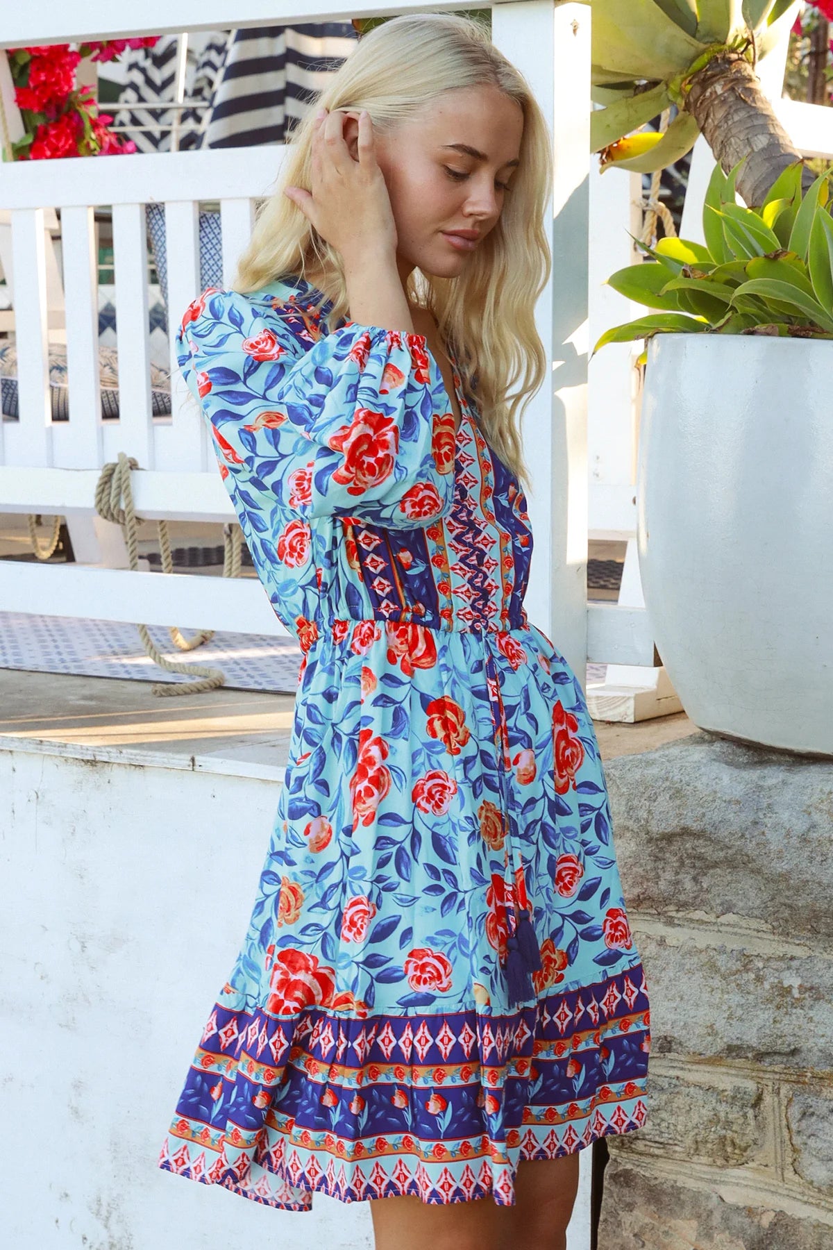Blonde woman in blue floral boho mini dress with red roses and border print details - Clarice Rose Mini Dress Bohemian Love Runway.