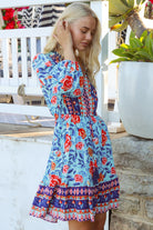 Blonde woman in blue floral boho mini dress with red roses and border print details - Clarice Rose Mini Dress Bohemian Love Runway.