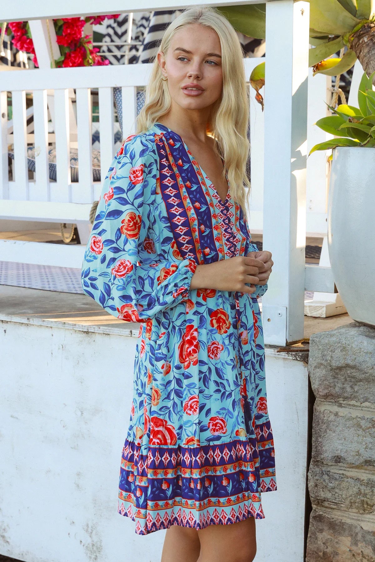 Blonde woman in blue floral boho mini dress with red roses and border print details - Clarice Rose Mini Dress Bohemian Love Runway.