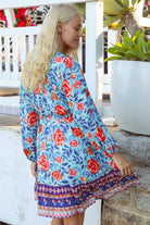 Blonde woman in blue floral boho mini dress with red roses and border print details - Clarice Rose Mini Dress Bohemian Love Runway.