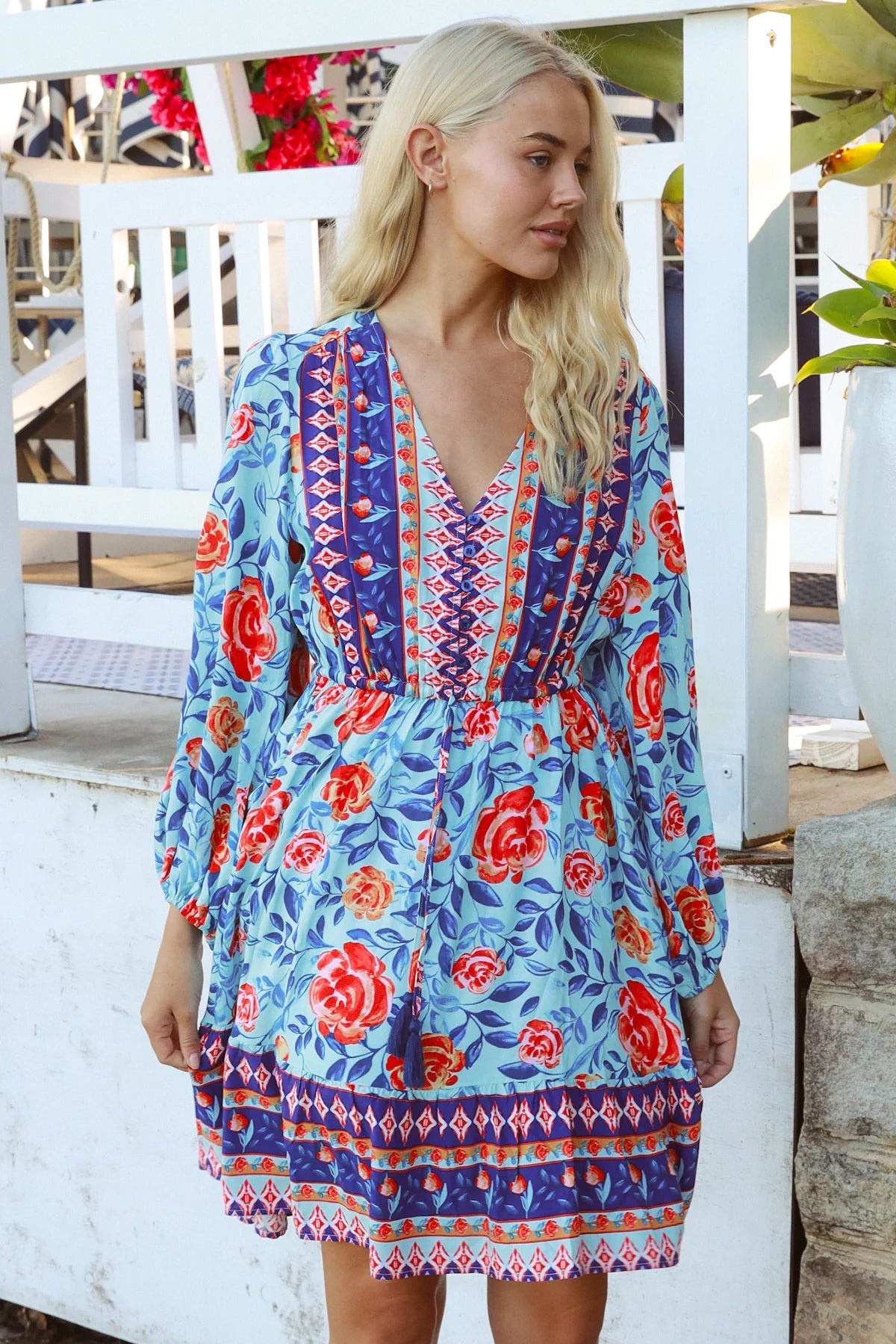 Blonde woman in blue floral boho mini dress with red roses and border print details - Clarice Rose Mini Dress Bohemian Love Runway.