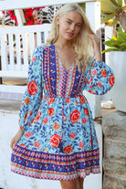Blonde woman in blue floral boho mini dress with red roses and border print details - Clarice Rose Mini Dress Bohemian Love Runway.