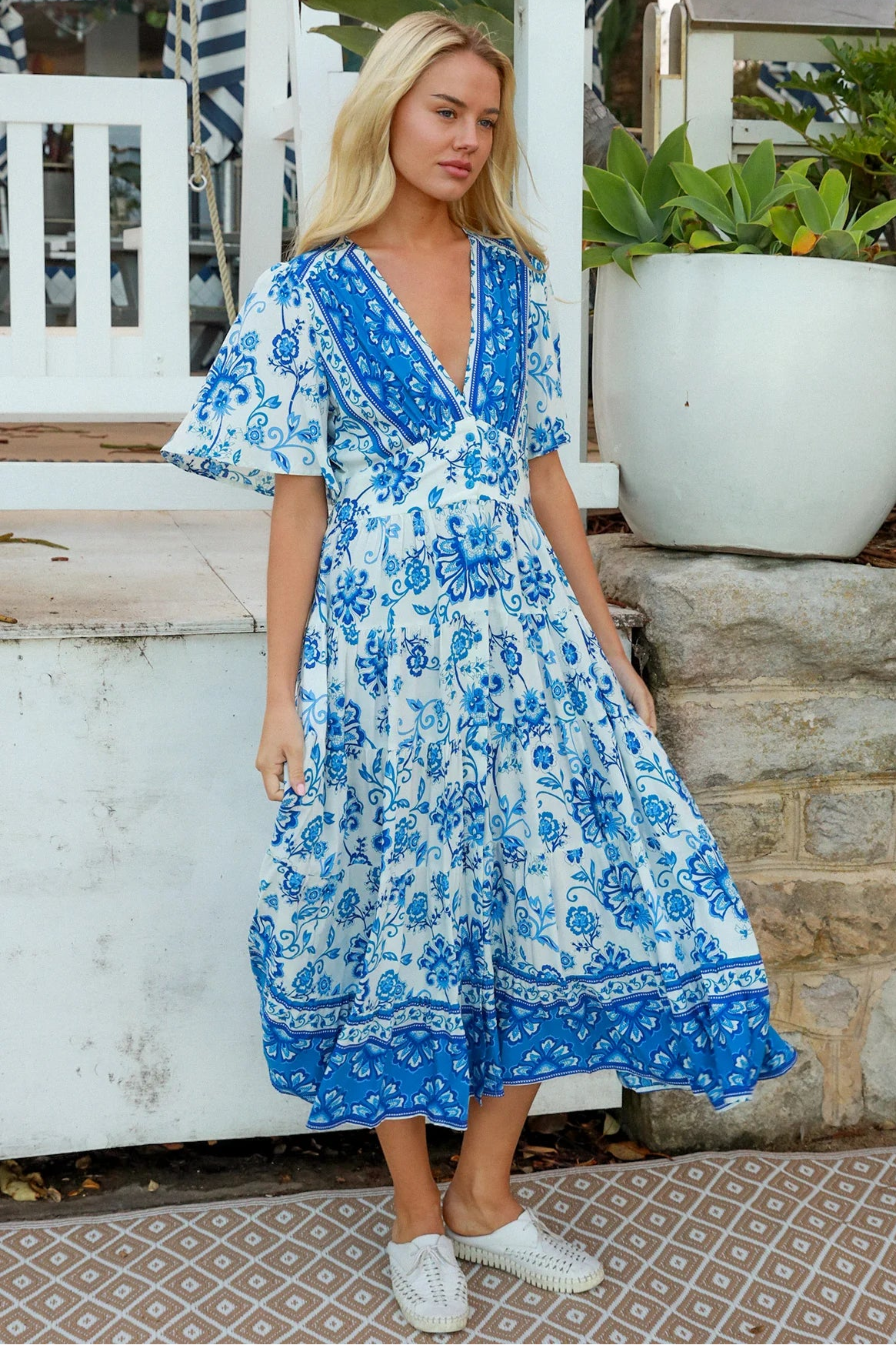 Woman in blue floral rayon bohemian midi dress with V-neckline flutter sleeves pockets and border frill hemline — Australia