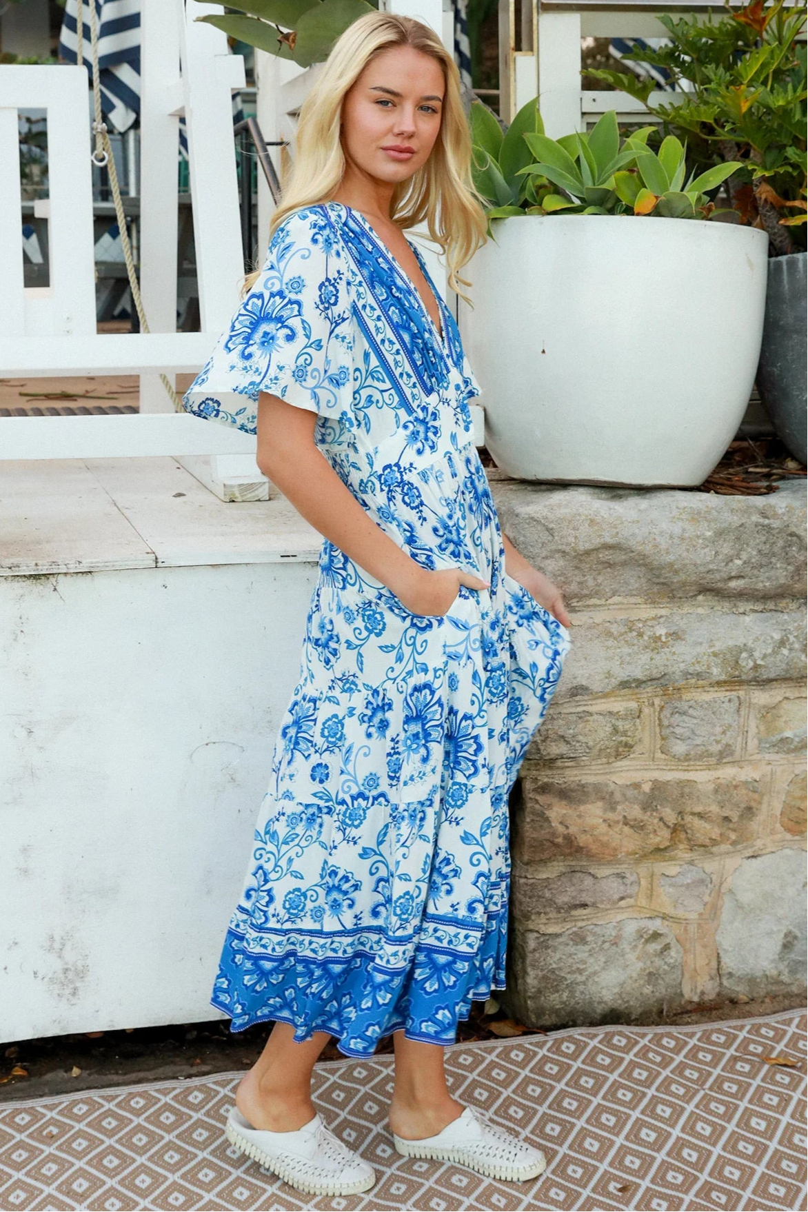 Woman in blue floral rayon bohemian midi dress with V-neckline flutter sleeves pockets and border frill hemline — Australia